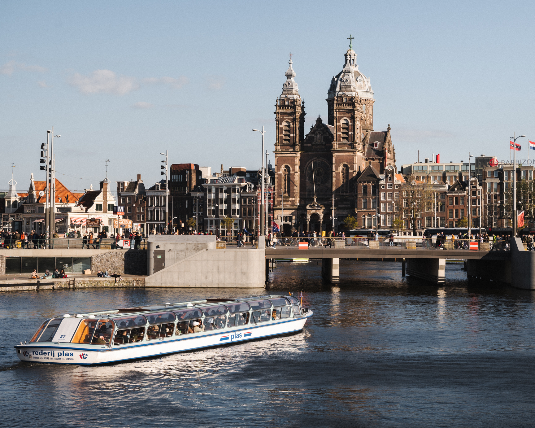 A photo of a cathedral right next to Amsterdam Centraal with a canal cruise going towards the bridge.